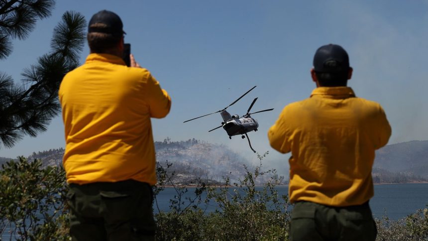 First responders look on as a firefighting helicopter prepares to take on water to battle the Thompson Fire on Wednesday.