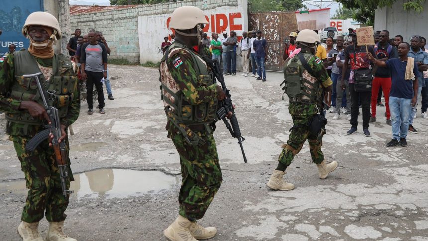 Kenyan police patrol an area near the international airport as a man holds a sign with a welcome message and a plea for jobs, in Port-au-Prince, Haiti, on July 3, 2024.