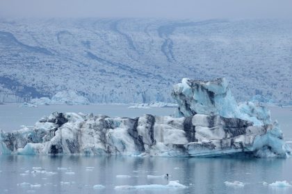 An iceberg that has broken off of receding Breidamerkurjokull glacier, which looms behind, floats on Jokulsarlon lake on August 15, 2021 near Hof, Iceland.