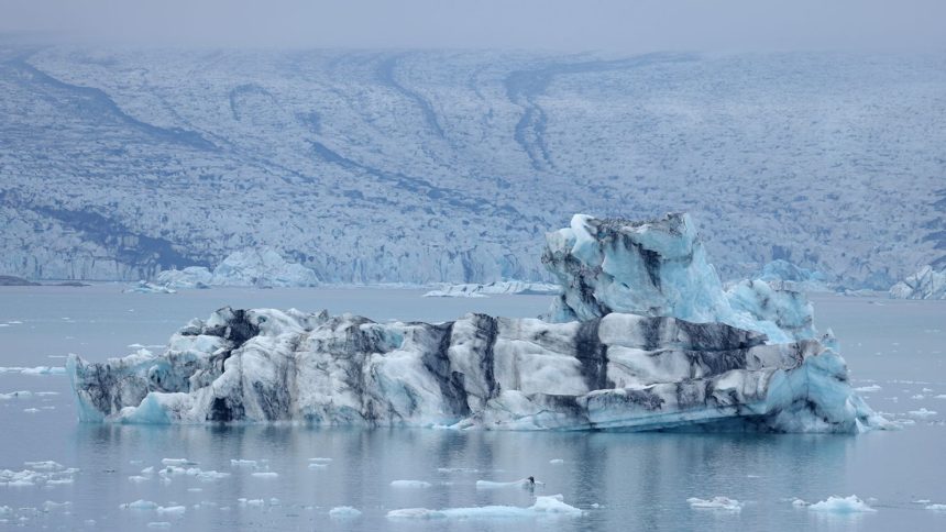 An iceberg that has broken off of receding Breidamerkurjokull glacier, which looms behind, floats on Jokulsarlon lake on August 15, 2021 near Hof, Iceland.