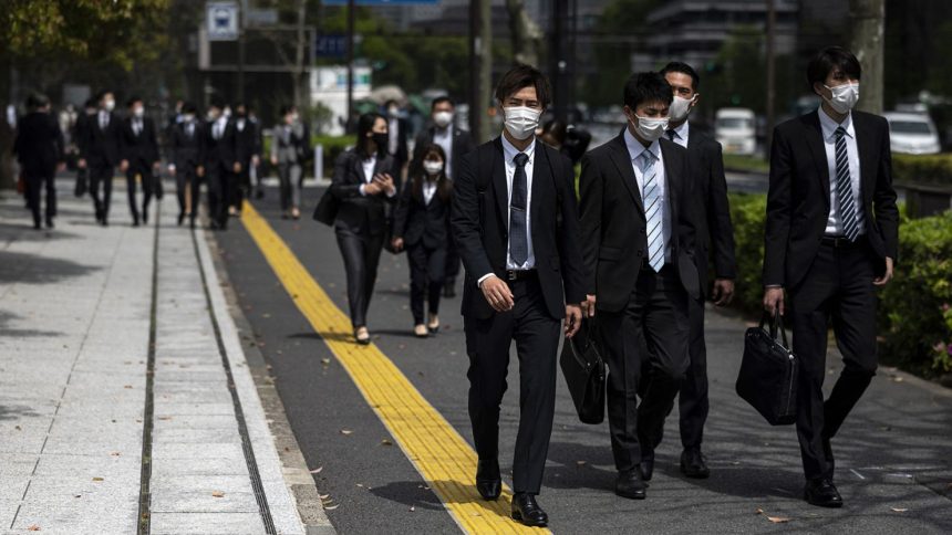 Pedestrians including office employees walk along a street in Tokyo's Kasumigaseki area at lunchtime on April 1, 2021.