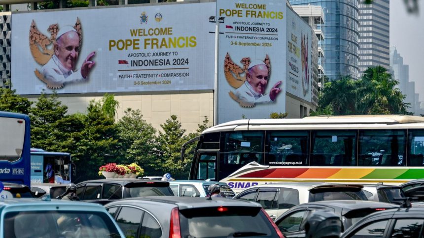 People drive their vehicles past giant billboards displaying a welcome message for Pope Francis in Jakarta's business district on September 2, 2024.