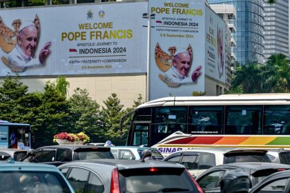 People drive their vehicles past giant billboards displaying a welcome message for Pope Francis in Jakarta's business district on September 2, 2024.