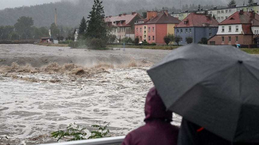 People shelter from the rain under umbrellas as they walk across a bridge over the Biala River in Glucholazy, southern Poland on Saturday.