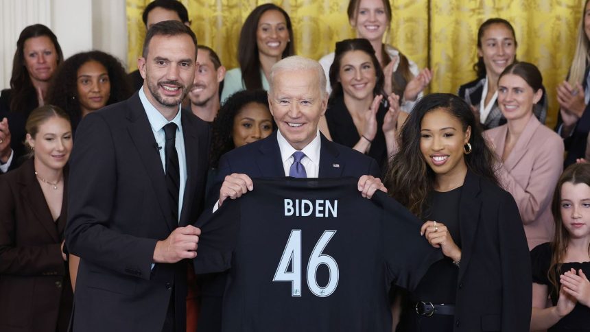 President Joe Biden is presented a jersey from NJ/NY Gotham FC head coach Juan Carlos Amorós and forward Midge Purce during a ceremony.