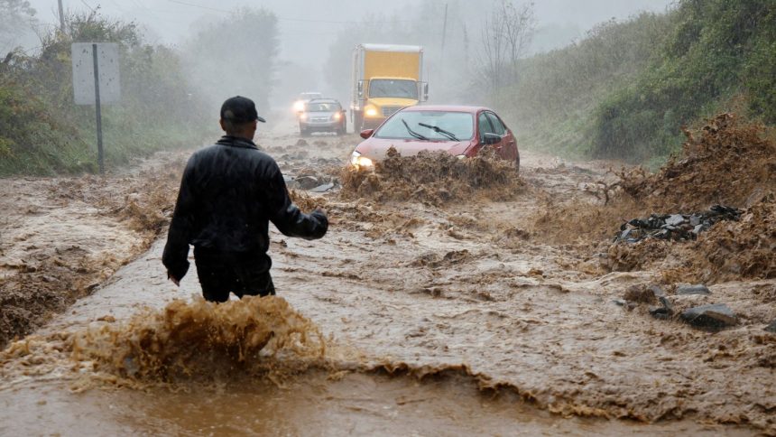 A person wades through fast-flowing floodwater on the outskirts of Boone, North Carolina, to assist a stranded driver as Helene strikes on September 27, 2024.