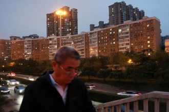 A man walks on a pedestrian bridge past residential buildings in Beijing, China, on October 16, 2024.