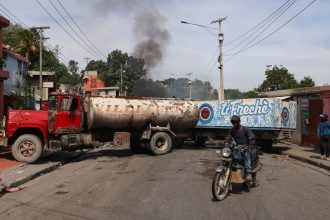 A motorcyclist drives around trucks blocking the road as heavily-armed gangs, which control most of the capital, fight for territory in Port-au-Prince, Haiti, on October 20, 2024.