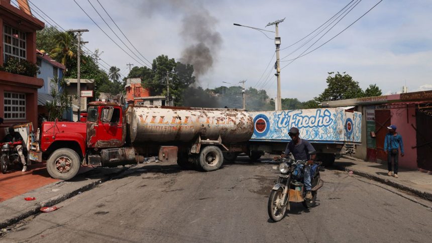 A motorcyclist drives around trucks blocking the road as heavily-armed gangs, which control most of the capital, fight for territory in Port-au-Prince, Haiti, on October 20, 2024.