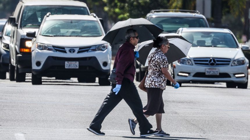 People cross the road amid hot weather in Covina, California, on Wednesday.