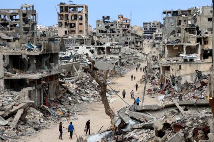 Palestinians walk on a dirt road lined with building rubble in the Shujaiya neighbourhood of Gaza City on October 7, 2024.