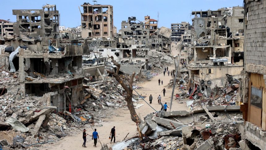 Palestinians walk on a dirt road lined with building rubble in the Shujaiya neighbourhood of Gaza City on October 7, 2024.