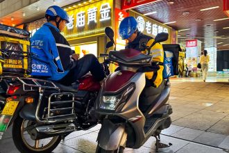 Food delivery riders from different companies wait on their scooters for their next orders on October 7, 2024 in Chongqing, China.