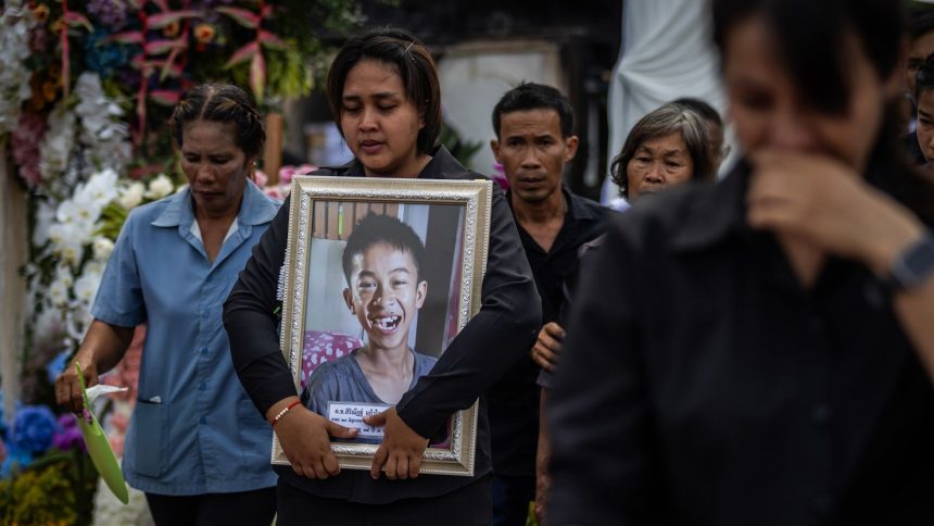 Family members of the victims hold photos of their loved ones during a mass cremation on October 8 for those who died in a bus fire during a school trip last week in Uthai Thani, Thailand.