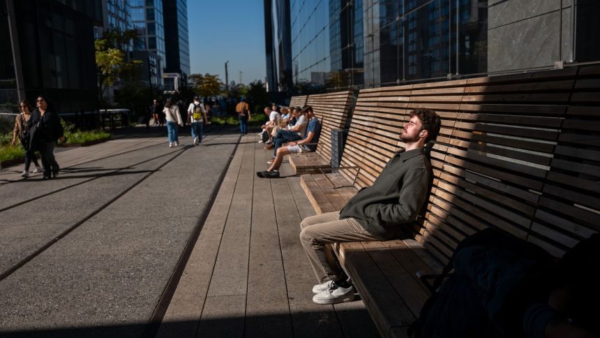 People rest in the sun along the High Line on a sunny and unusually warm day in New York City on October 21, 2024.