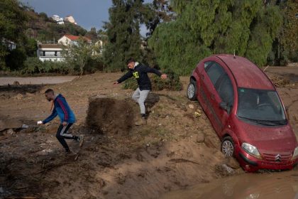 Men run next to a car covered with mud on a flooded street in Alora, near Malaga, on October 29, 2024, after a heavy rain hit southern Spain.