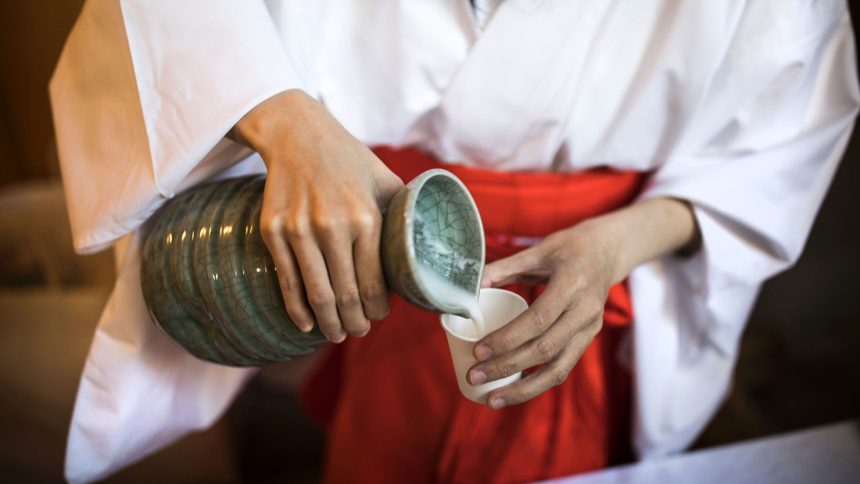 A Japanese attendant pours sake into a cup for visitors at the Koami Shinto shrine.