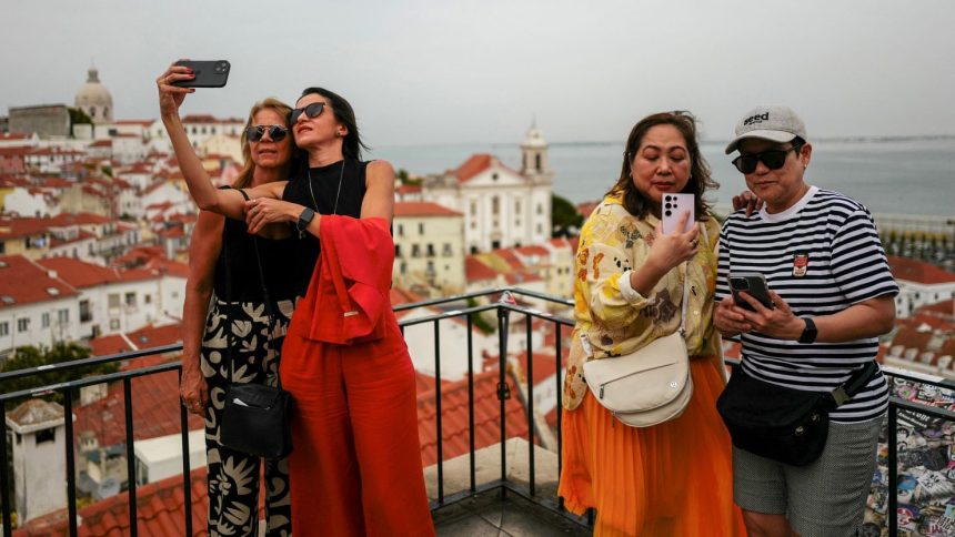 Thousands of locals in Lisbon, Portugal have signed a petition demanding the city cuts down on its tourist lets. Pictured here: people take photos from a popular viewpoint in Lisbon's Alfama neighborhood.