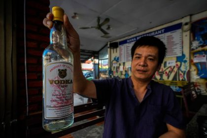 The manager of a hostel in Vang Vieng displays a bottle of Tiger Vodka in Vang Vieng, Laos, on November 19, 2024.