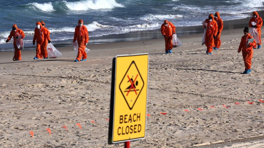 Workers in protective suits conduct a clean-up operation to clear mysterious black balls that washed ashore on Coogee Beach in Sydney, Australia on October 17, 2024.