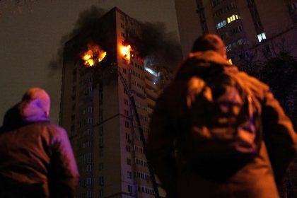 People look at Ukrainian firefighters working to put out a fire in a high-rise residential building after being reportedly hit by a drone, in Kyiv, on October 25, 2024.