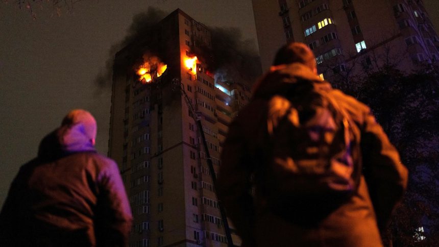 People look at Ukrainian firefighters working to put out a fire in a high-rise residential building after being reportedly hit by a drone, in Kyiv, on October 25, 2024.