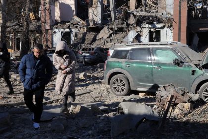 Local residents and a policeman walk next to damaged cars in the courtyard of a destroyed building following a missile attack in Odesa on November 25, 2024.