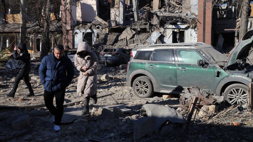 Local residents and a policeman walk next to damaged cars in the courtyard of a destroyed building following a missile attack in Odesa on November 25, 2024.