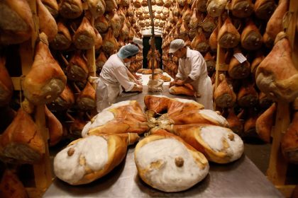 Employees grease hams with lard before hanging them to dry in storage as part of the Parma ham curing process at Pio Tosini Industria Prosciutti in Langhirano, Italy.