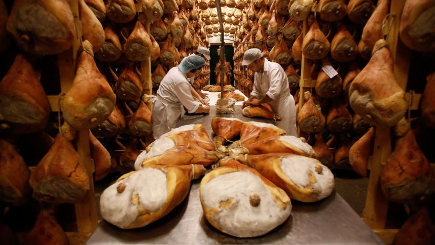 Employees grease hams with lard before hanging them to dry in storage as part of the Parma ham curing process at Pio Tosini Industria Prosciutti in Langhirano, Italy.