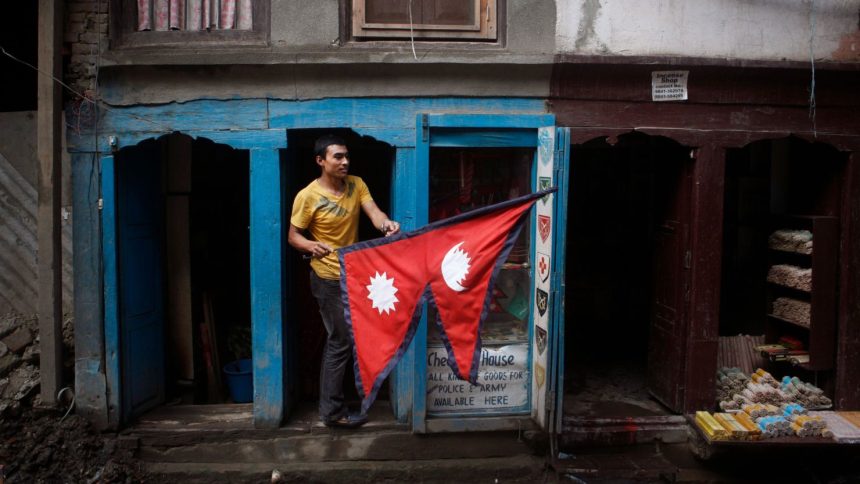 A man carries a Nepali flag as he stands outside his stall in Kathmandu.