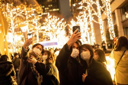 Couples take selfies on a street with Christmas lights in Tokyo on December 25, 2022.