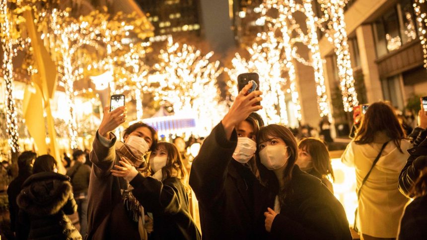 Couples take selfies on a street with Christmas lights in Tokyo on December 25, 2022.