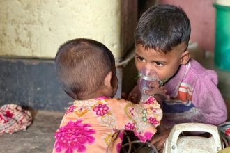 Siblings Chahat, 3 (right) and Diya, 1, play with a nebulizer in their one-room home in a slum in Delhi in November while pollution soars outside.