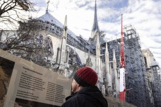 A tourist in front of Notre Dame de Paris Cathedral on the eve of the official reopening five years after the 2019 fire that ravaged the monument.