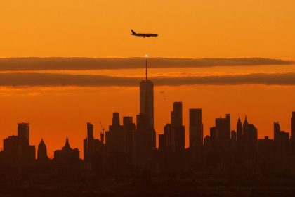 A plane approaching Newark Liberty International Airport flies over lower Manhattan in New York as the sun rises October 22, 2023.