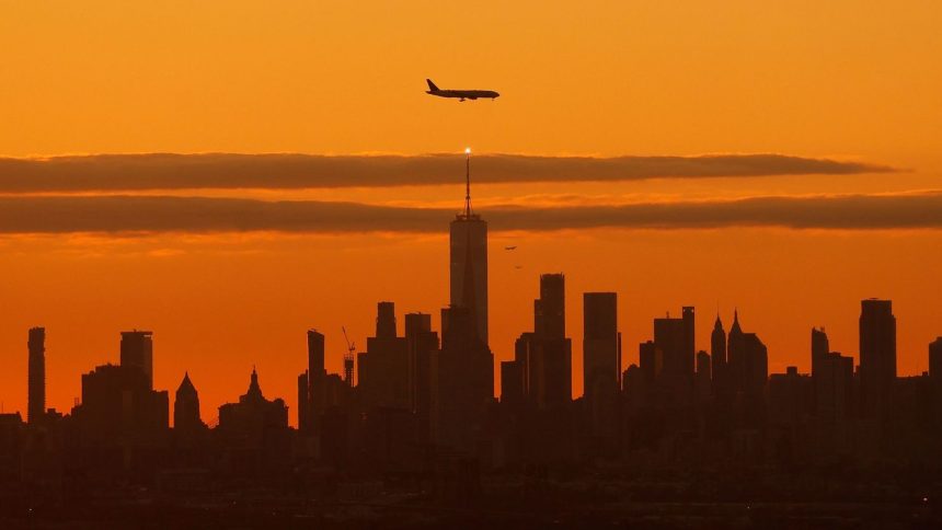 A plane approaching Newark Liberty International Airport flies over lower Manhattan in New York as the sun rises October 22, 2023.