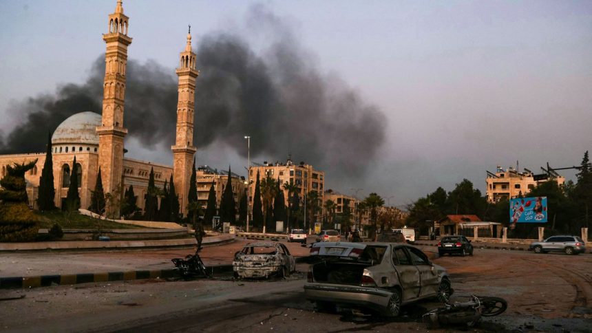 Smoke billows in the distance as damaged cars are seen at the site of Syrian regime airstrikes targeting opposition fighters in Aleppo, in northern Syria, on November 30, 2024.