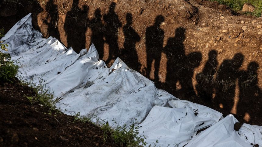 Residents cast their shadows as they observe members of the Congolese Red Cross conduct a mass burial for victims of the clashes in eastern Democratic Republic of Congo at Musigiko cemetery in Bukavu on February 20, 2025.