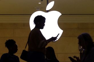 FILE PHOTO: A women uses an iPhone mobile device as she passes a lighted Apple logo at the Apple store at Grand Central Terminal in New York City, U.S., April 14, 2023. REUTERS/Mike Segar/File Photo