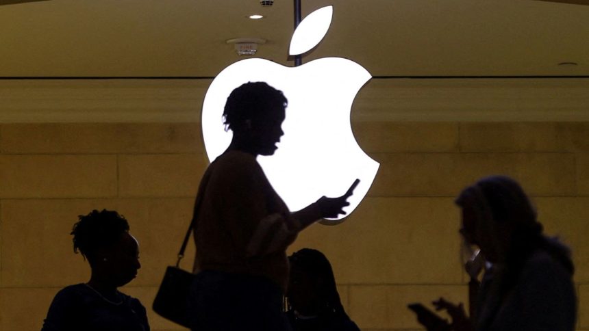 FILE PHOTO: A women uses an iPhone mobile device as she passes a lighted Apple logo at the Apple store at Grand Central Terminal in New York City, U.S., April 14, 2023. REUTERS/Mike Segar/File Photo