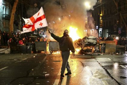 A man waves a Georgian national flag in front of a burning barricade not far from the parliament building in Tbilisi, Georgia on Thursday, March 9, 2023.