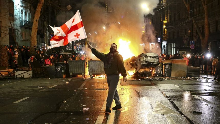 A man waves a Georgian national flag in front of a burning barricade not far from the parliament building in Tbilisi, Georgia on Thursday, March 9, 2023.