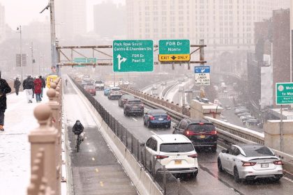 People walk along the Brooklyn Bridge as cars drive into Manhattan on January 6 in New York.