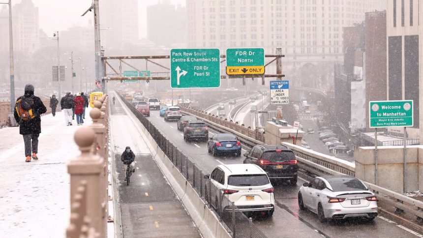 People walk along the Brooklyn Bridge as cars drive into Manhattan on January 6 in New York.