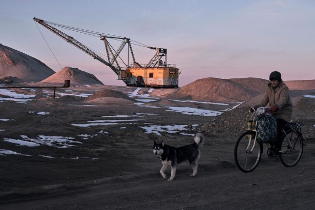 A woman cycles past with her dog as an excavator mines on February 25, in the Zhytomyr region of Ukraine.