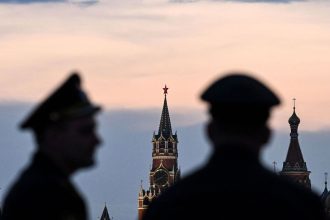 Russian servicemen stand with the Kremlin's Spasskaya tower and Saint Basil's cathedral before the Victory Day military parade rehearsal in central Moscow, on April 27, 2023.