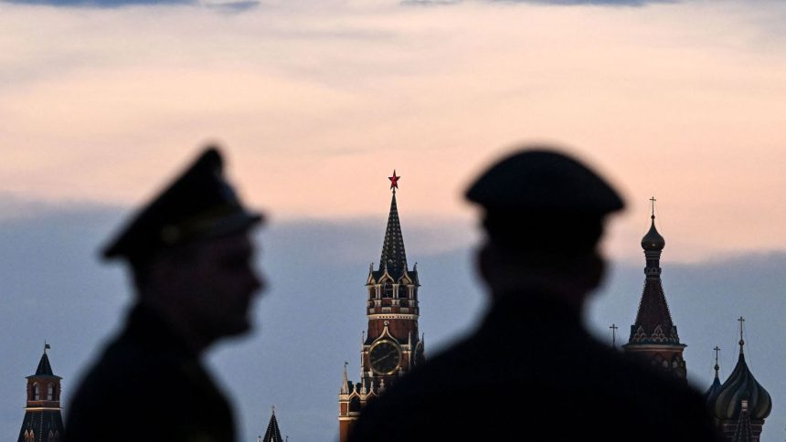 Russian servicemen stand with the Kremlin's Spasskaya tower and Saint Basil's cathedral before the Victory Day military parade rehearsal in central Moscow, on April 27, 2023.