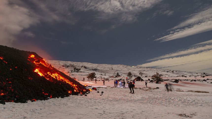 A crowd of tourists gather to witness a lava flow descend down the southwestern flank of Mount Etna.