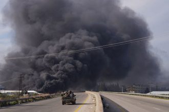 Smoke rises while members of the Syrian forces ride on a vehicle as they battle against an insurgency by fighters loyal to ousted leader Bashar al-Assad's Alawite sect, in Latakia, Syria, on March 7.